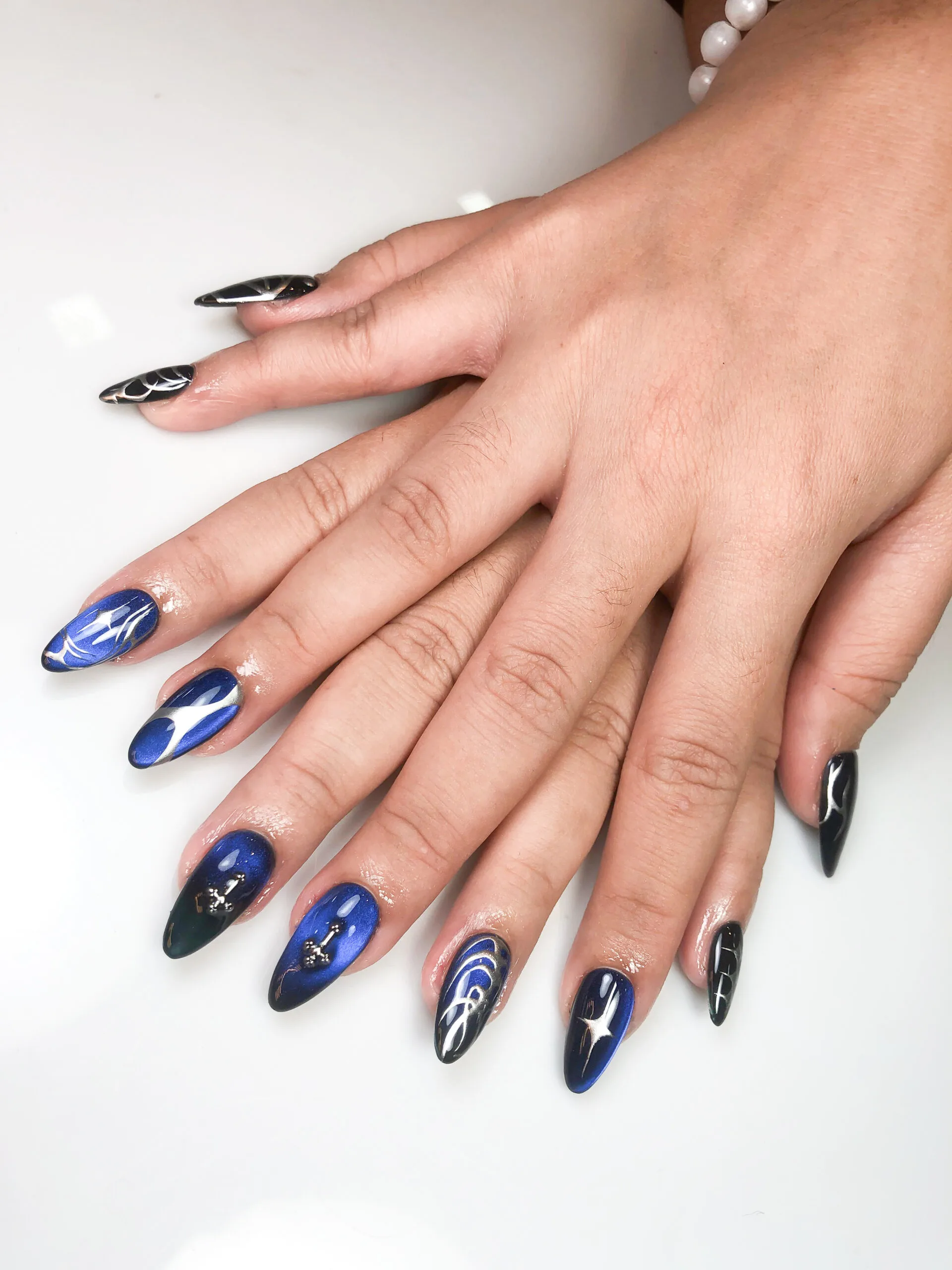 Nail art almond biru gelap glossy dengan aksen line art
